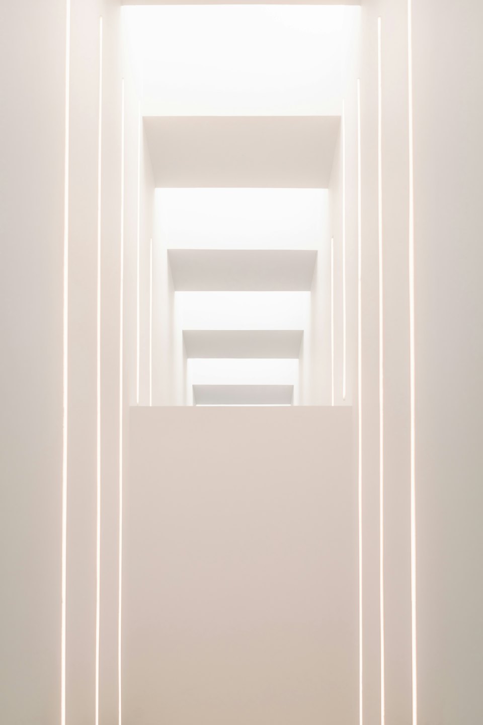 Moderno corridoio bianco con illuminazione lineare verticale integrata.